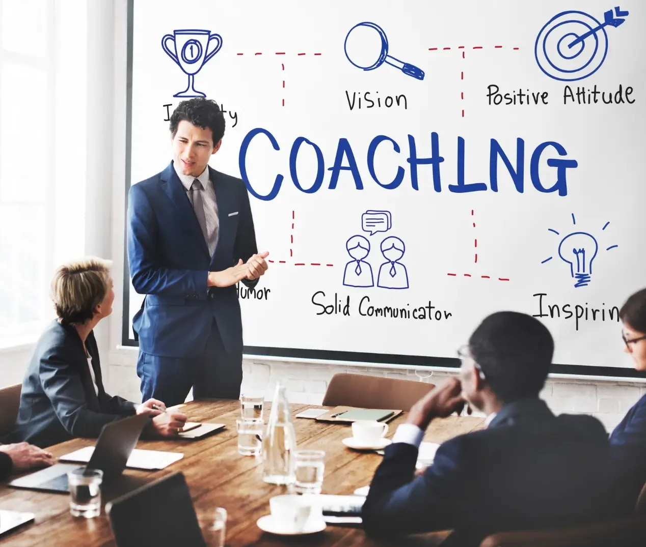 Coach presenting to team beside whiteboard graphic about coaching skills.