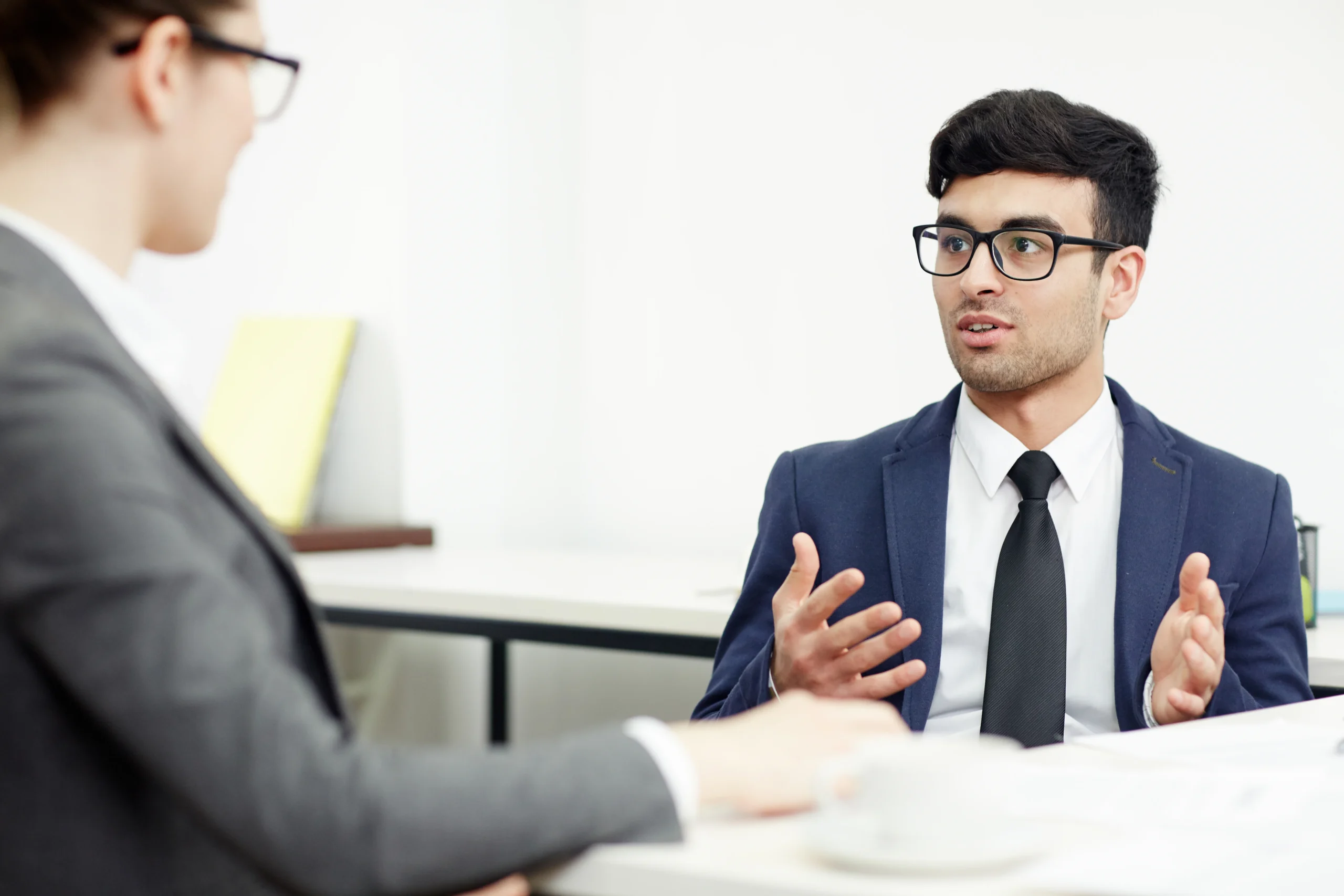 Young professional explaining points in interview-style meeting across desk.