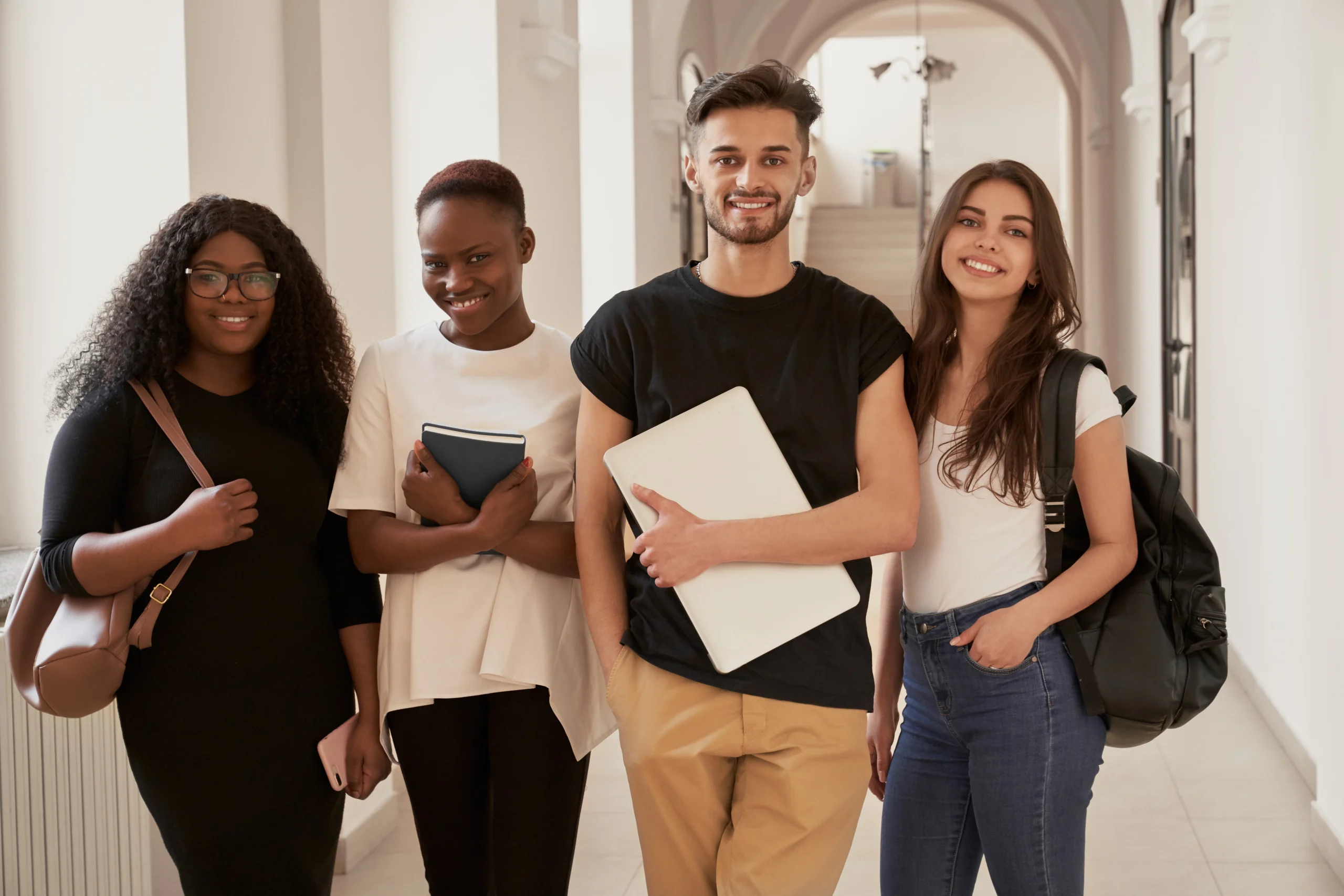 Smiling university students standing in corridor with backpacks and notebooks.